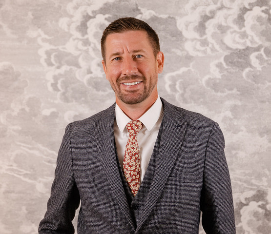 A man (Ben) Smiling in a grey suit with a red tie.