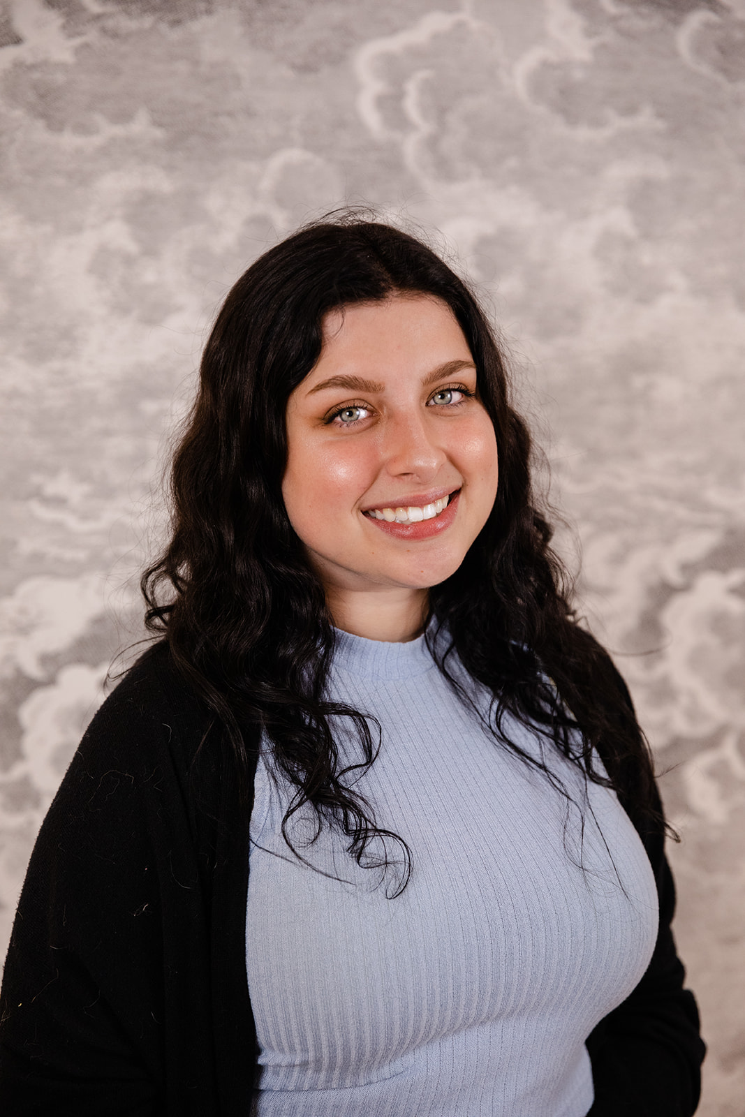 A girl (Sara) smiling, wearing a blue shirt with a black cardigan. She has black hair.