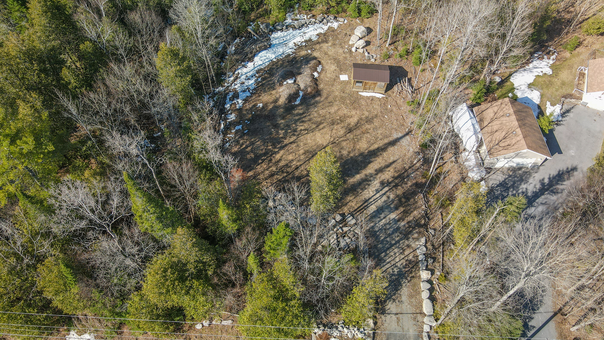 Bird's eye view of vacant lot, with a driveway and a small wooden shed at the back of the lot.